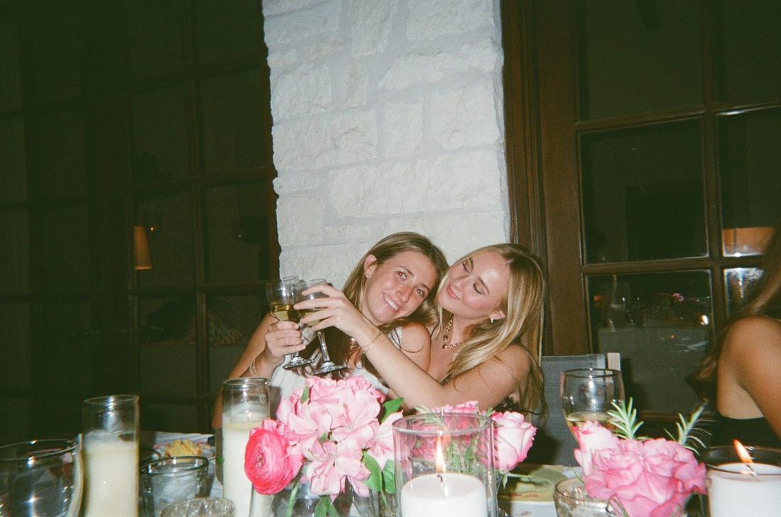 Two friends clinking glasses over pink roses